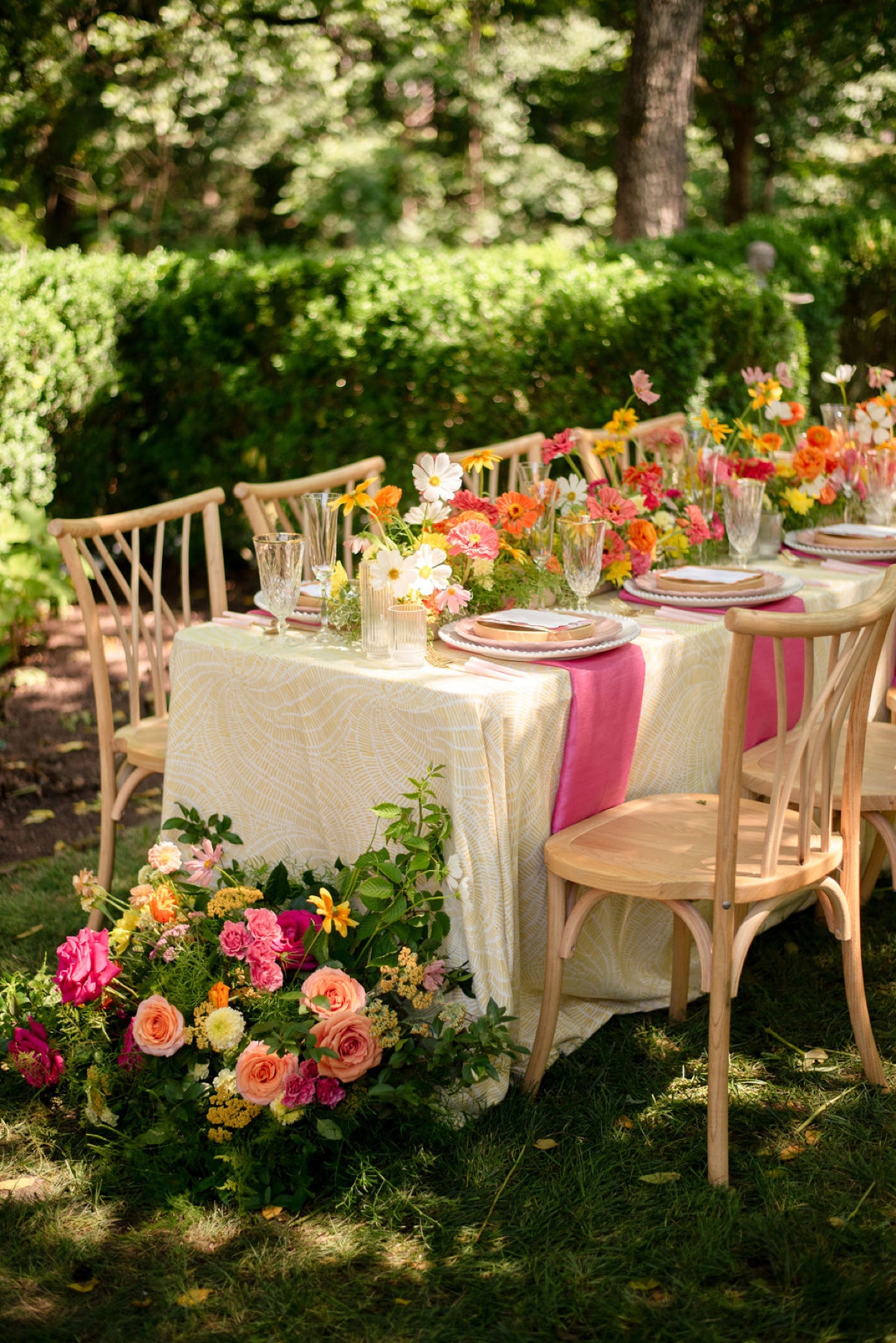 Hot pink and yellow grounded floral arrangement next to an outdoor dining table with natural wood bistro chairs