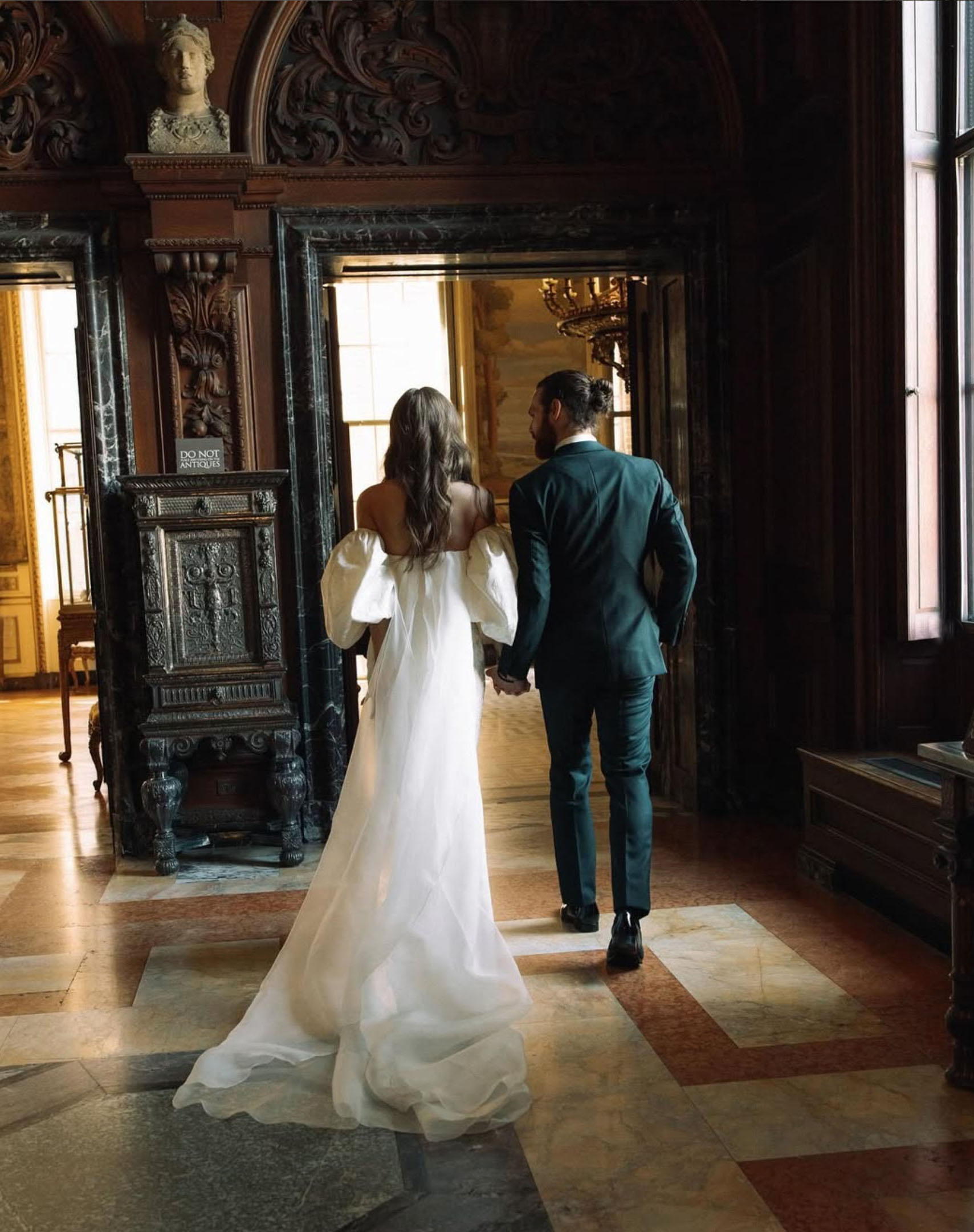 Bride and groom walking hand in hand through the ornate interior hallway showcasing dark wood paneling, marble flooring, and gilded details