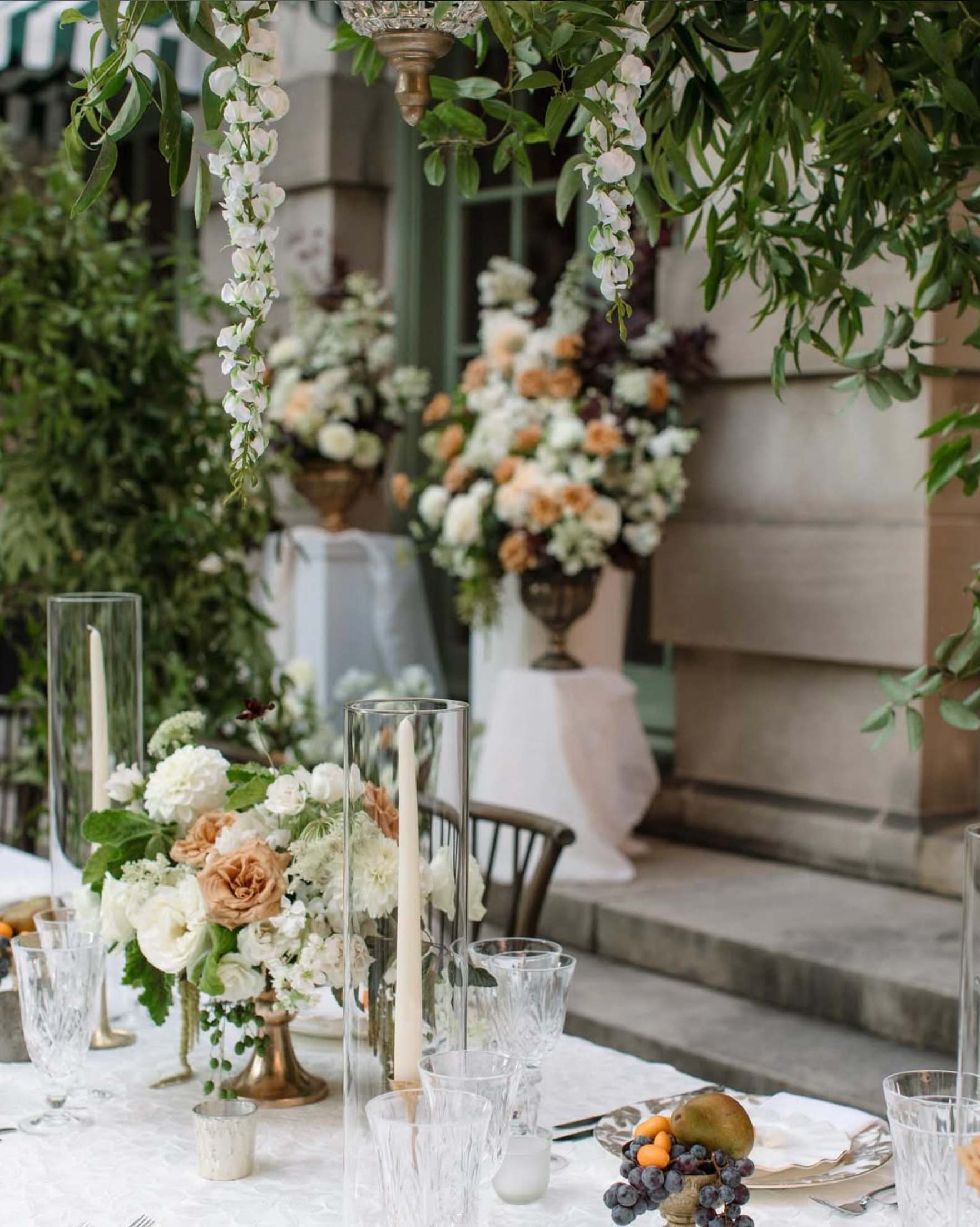 Harvest-inspired wedding table featuring sliced pears, blackberries, white taper candles, and lush floral arrangements under hanging greenery