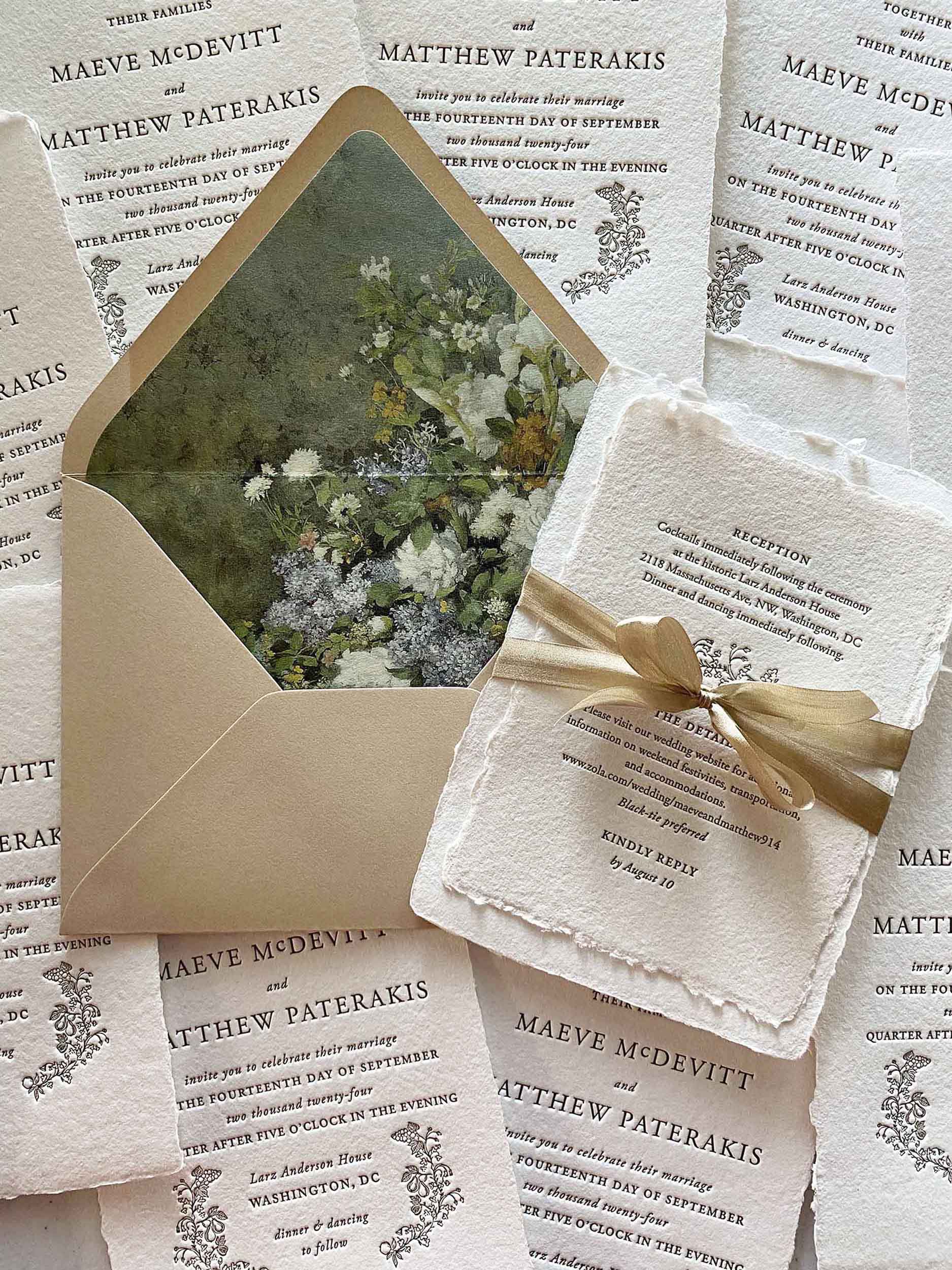 Flat lay of custom letterpress wedding invitations on handmade paper with a vintage botanical envelope liner, tied with a gold ribbon.