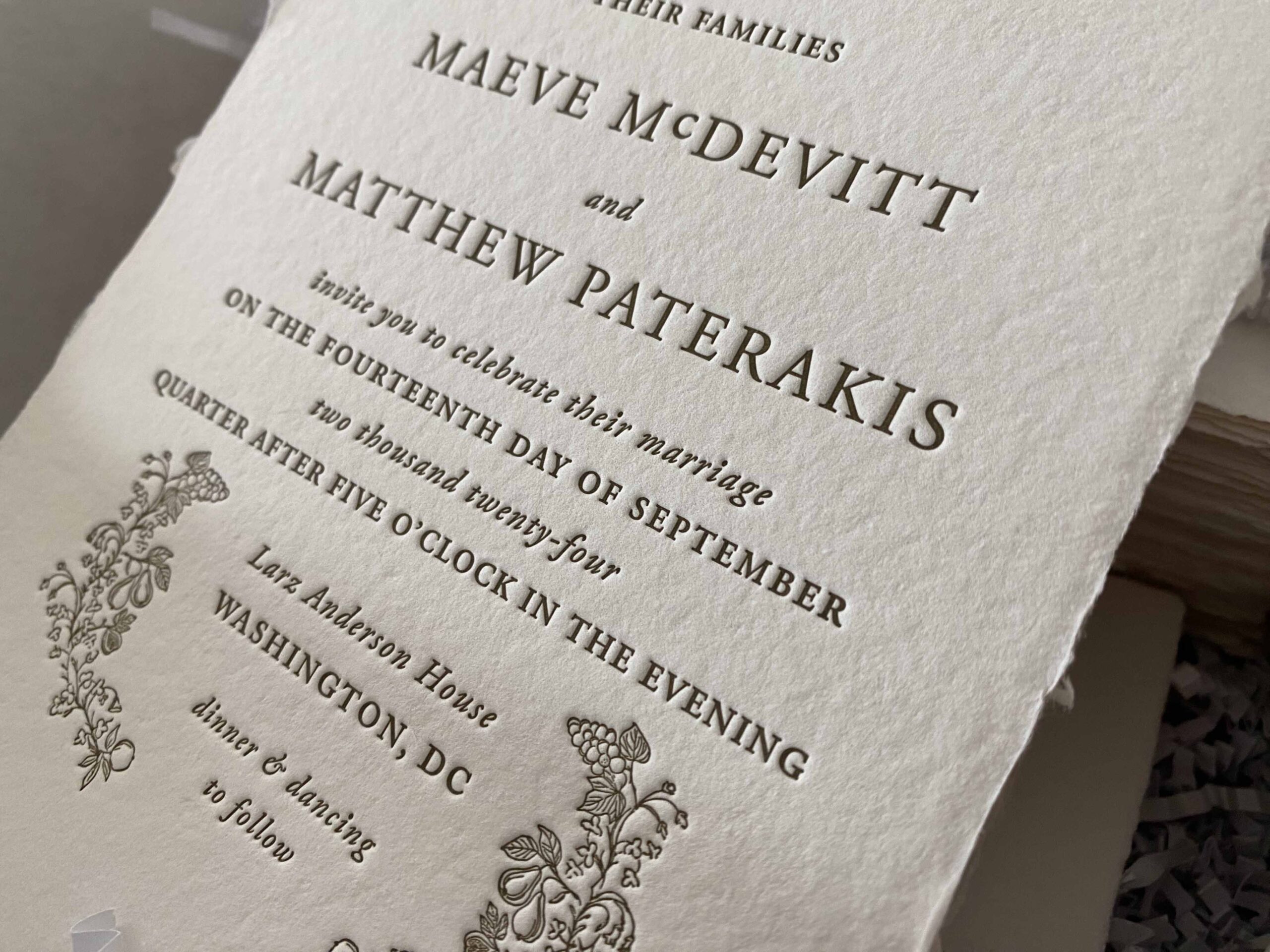 Close-up of a custom letterpress wedding invitation on handmade paper, featuring embossed serif lettering and vintage botanical accents.