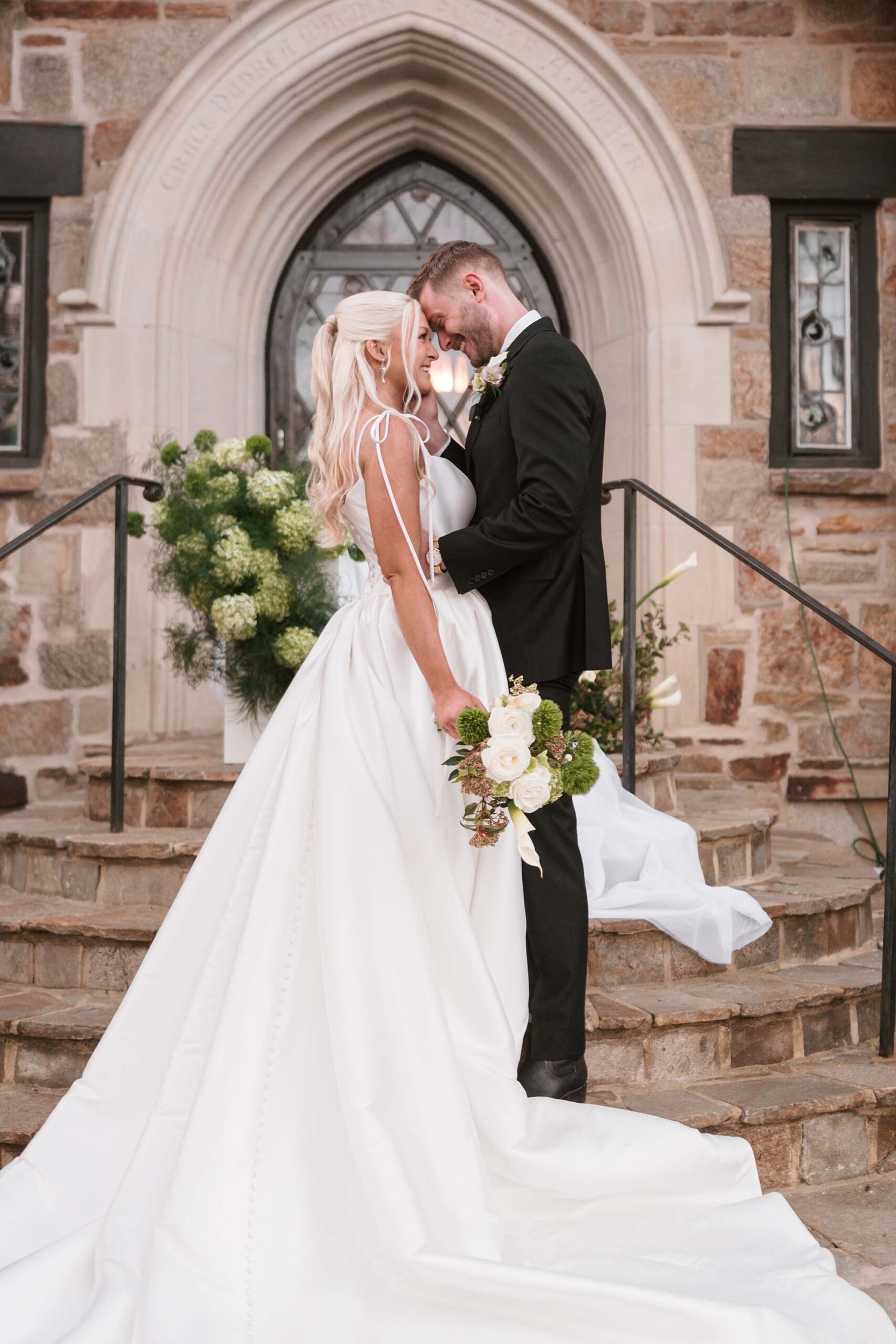 Bride and groom embracing forehead to forehead in front of a gothic-style castle entrance