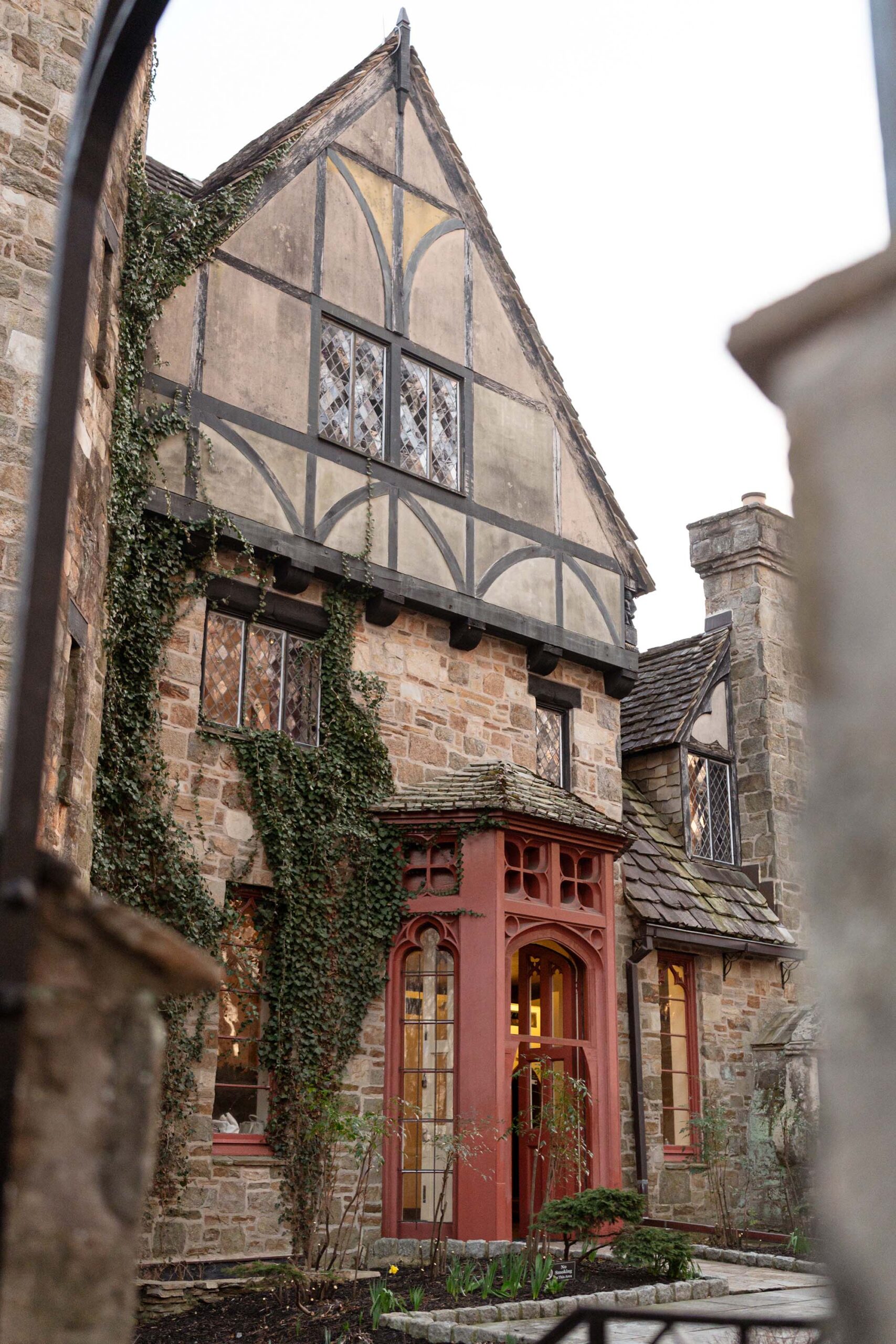 Tudor-style entrance of a castle wedding venue with red gothic arches and lush ivy accents.