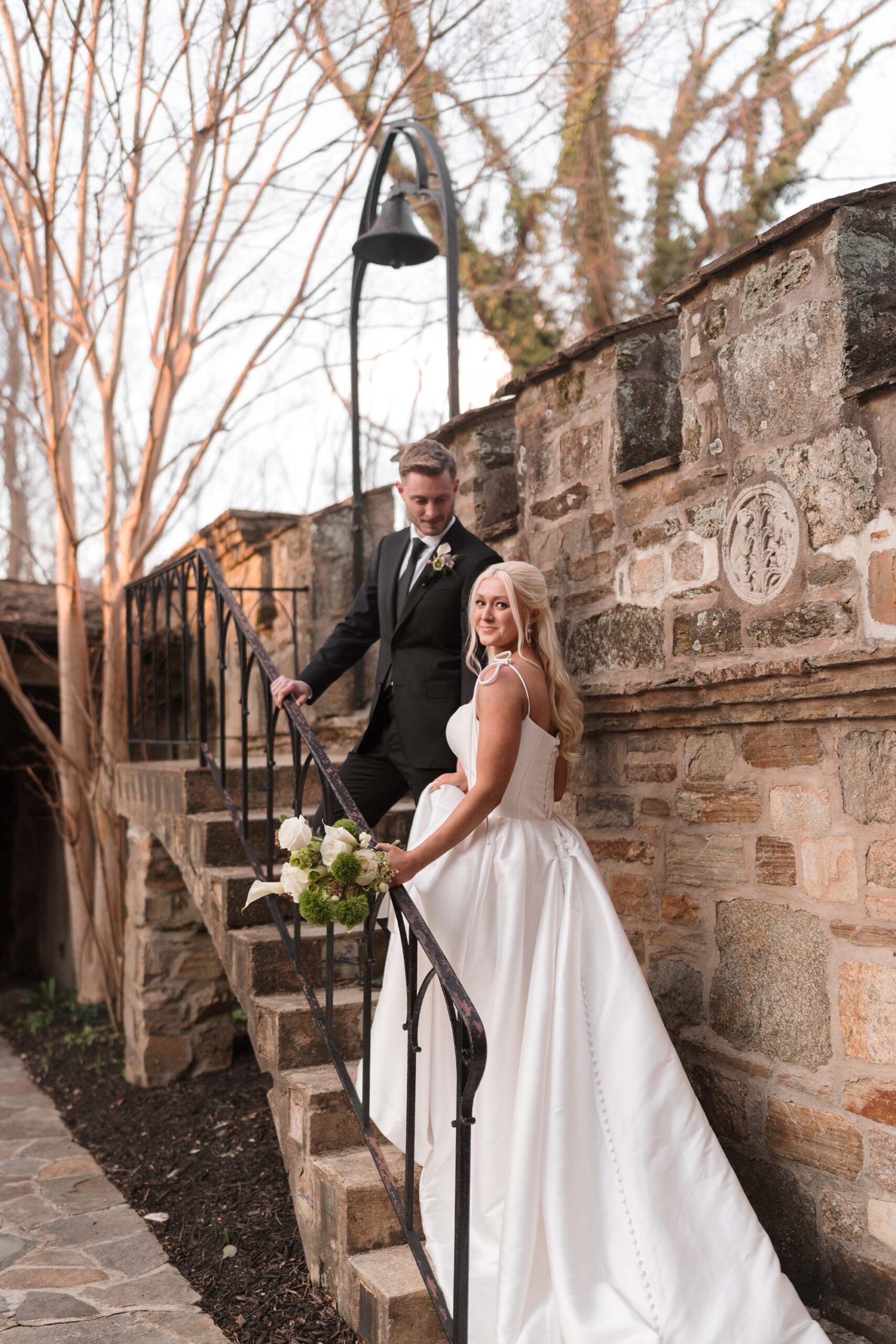 Bride looks over her shoulder while ascending the stairs with her groom at Cloisters Castle in Maryland.