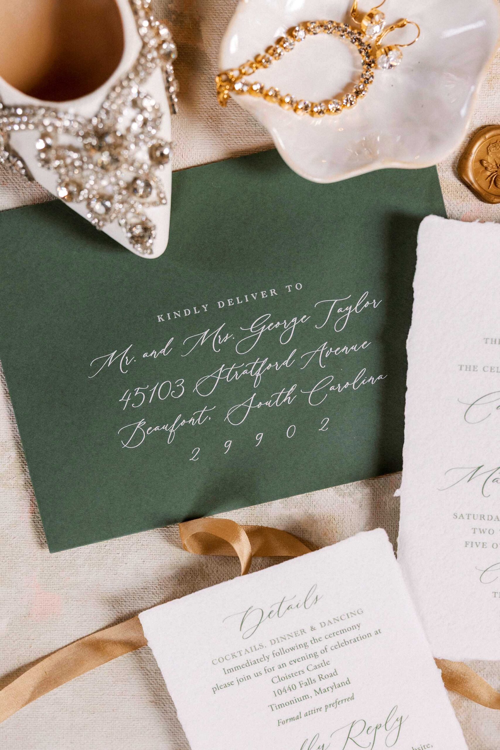 Flatlay of wedding invitation with green envelope and gold ribbon