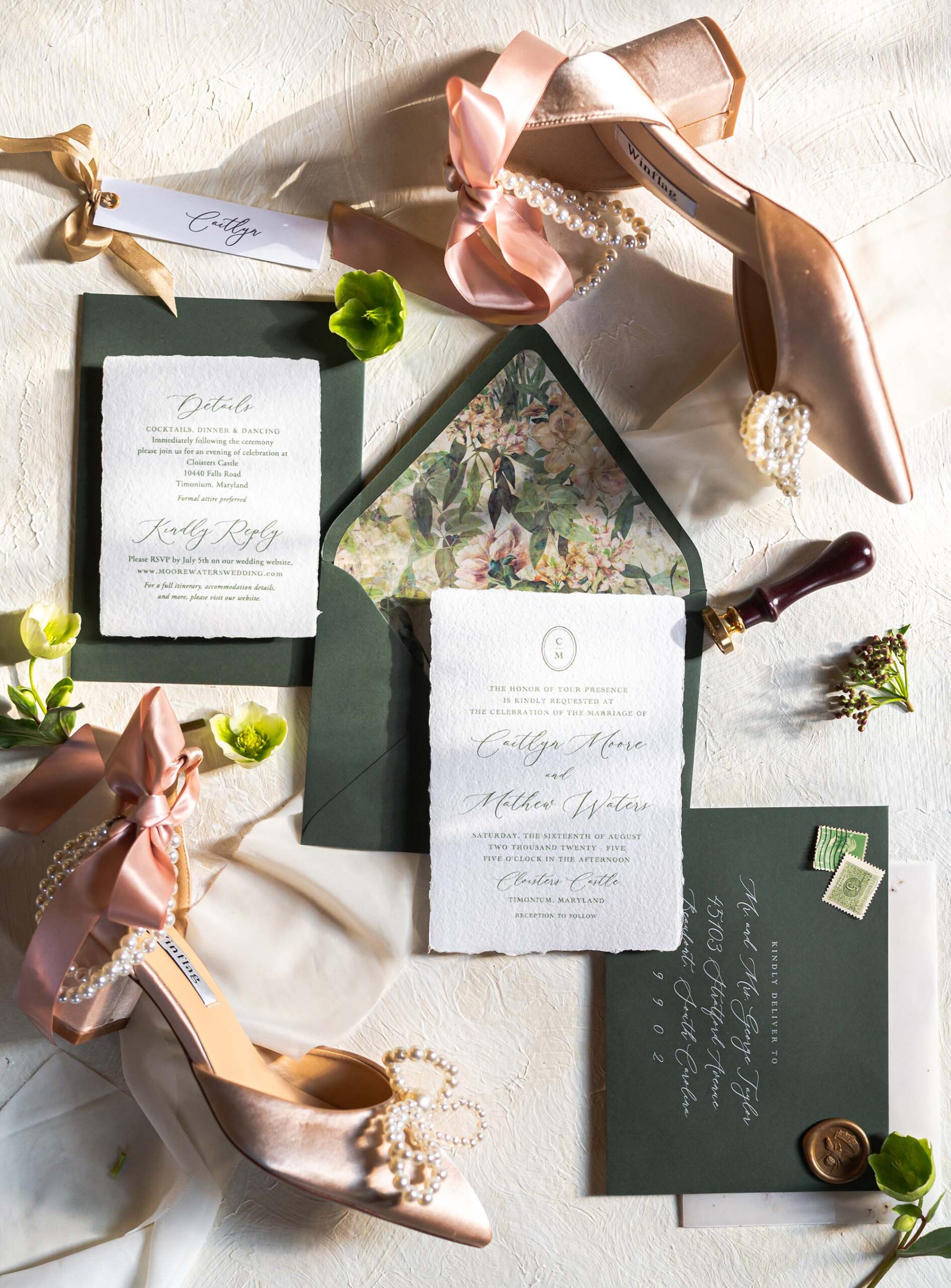 Green and blush floral wedding invitation suite styled with pearl heels and satin ribbon for a romantic flatlay.