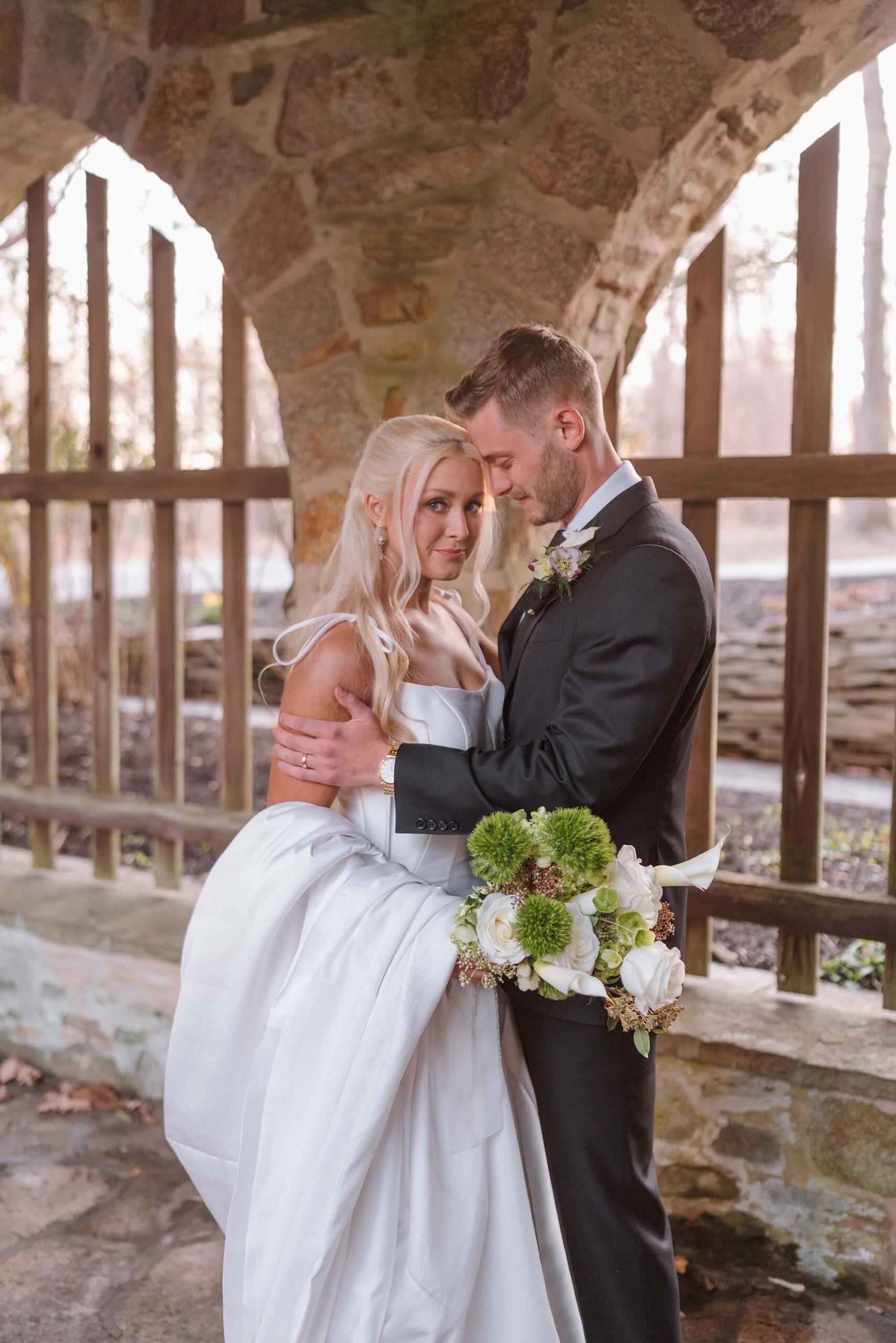 Bride and groom sharing an intimate moment under the stone arches at Cloisters Castle, framed by rustic architecture and soft afternoon light.