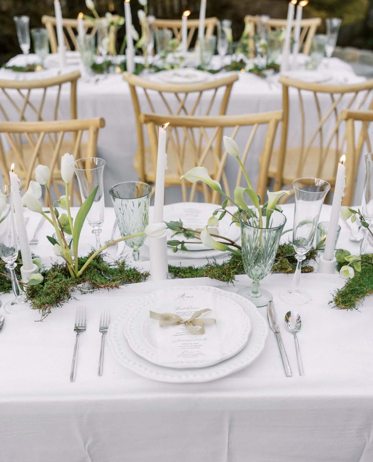 Elegant wedding reception tablescape with white tulips, moss runner, taper candles, and linen menus at The Cloisters Castle in Maryland