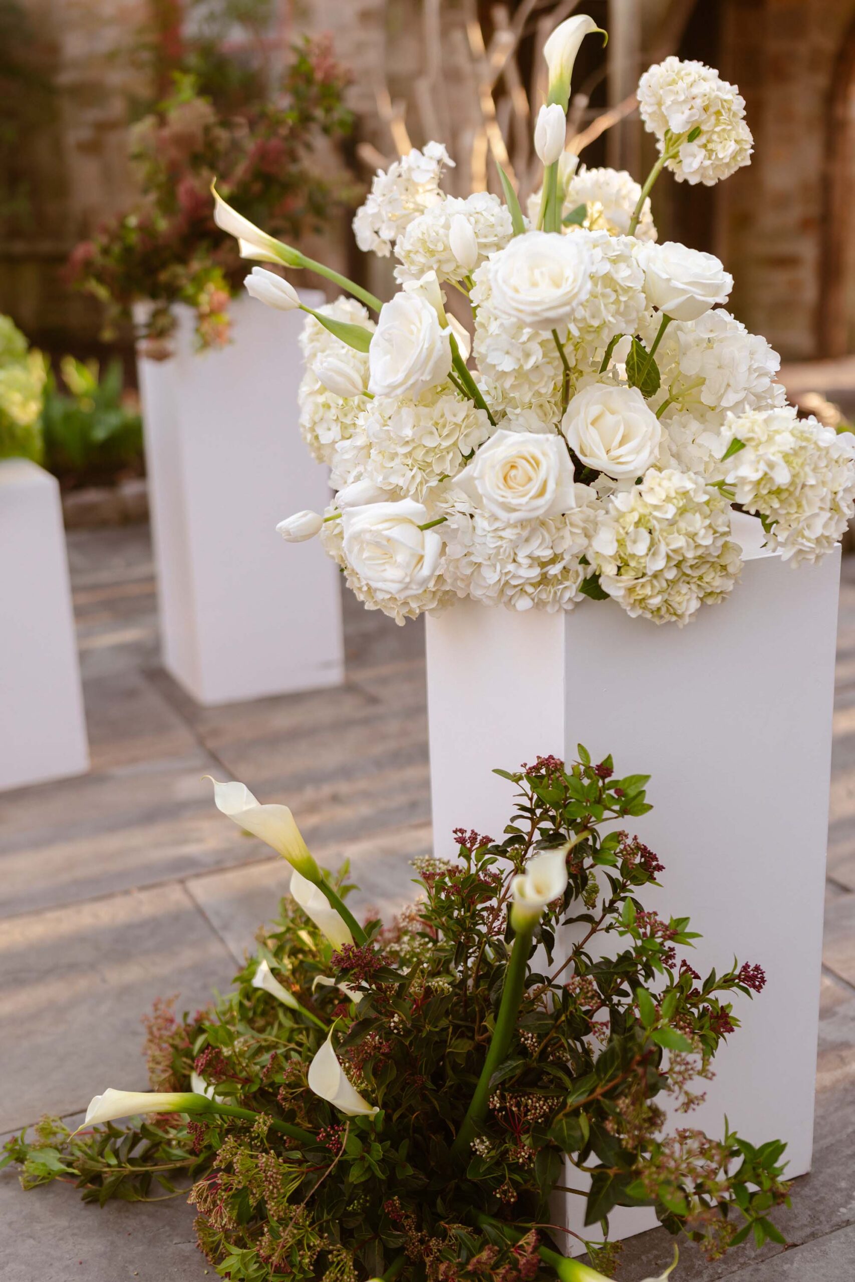 Elegant white wedding flowers including hydrangeas, roses, and tulips arranged on tall white pedestals for a castle ceremony.
