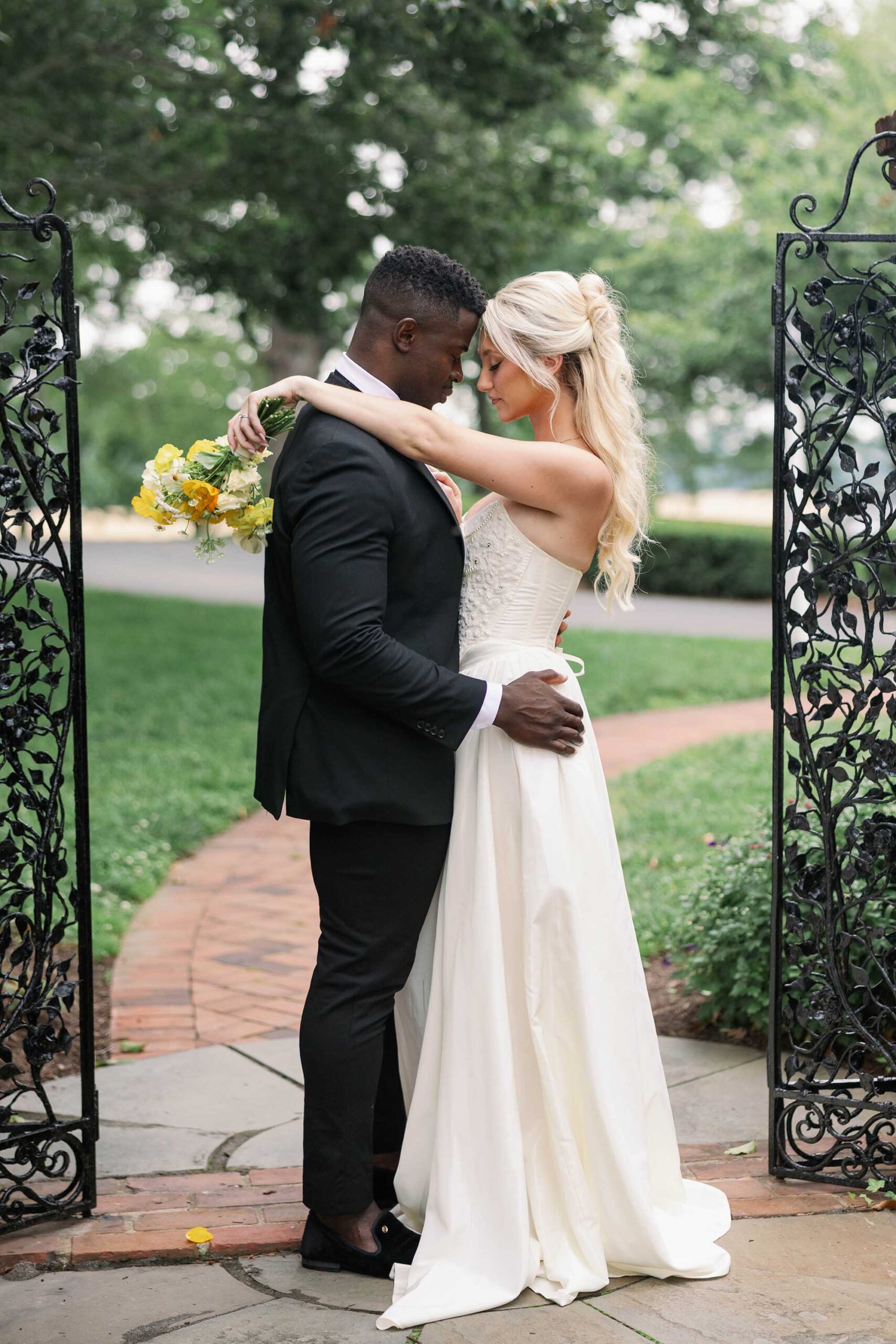 Romantic bride and groom embrace at the garden gates of Brittland Estates, styled with Italian-inspired wedding florals and elegant attire.