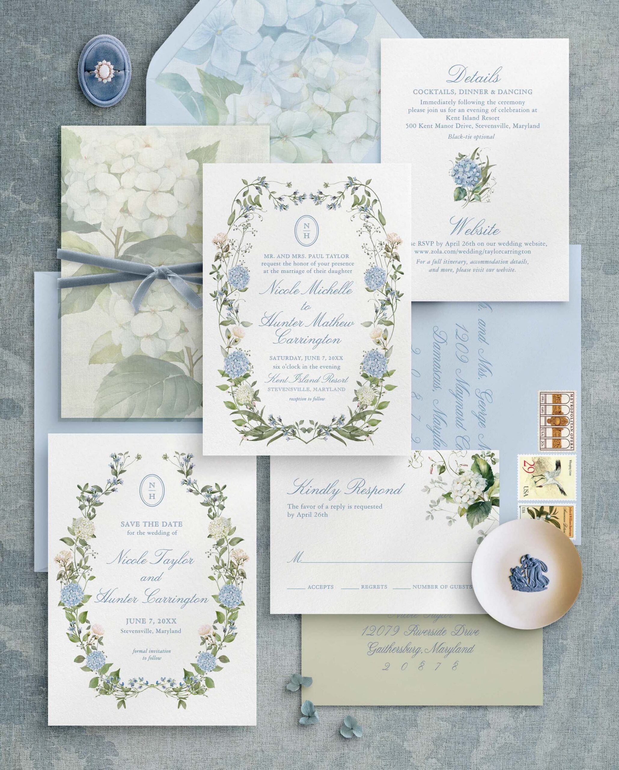 Flat lay of blue hydrangea wedding invitations with monogram crest, save the date, RSVP card, envelopes and details card styled with ring box and stamps.