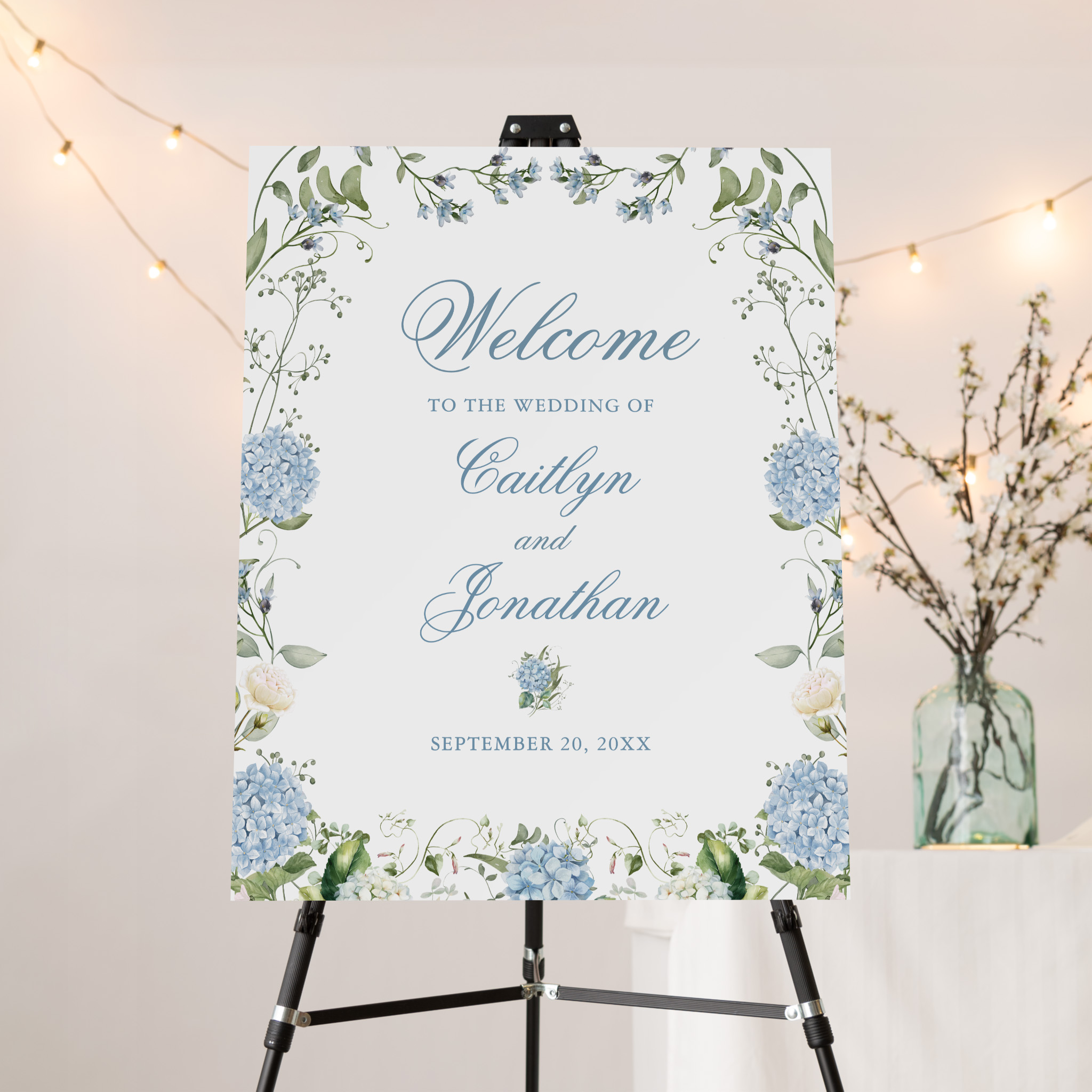 Welcome to the wedding sign framed with blue hydrangeas and greenery, featuring couple’s names and date in blue script on white background.