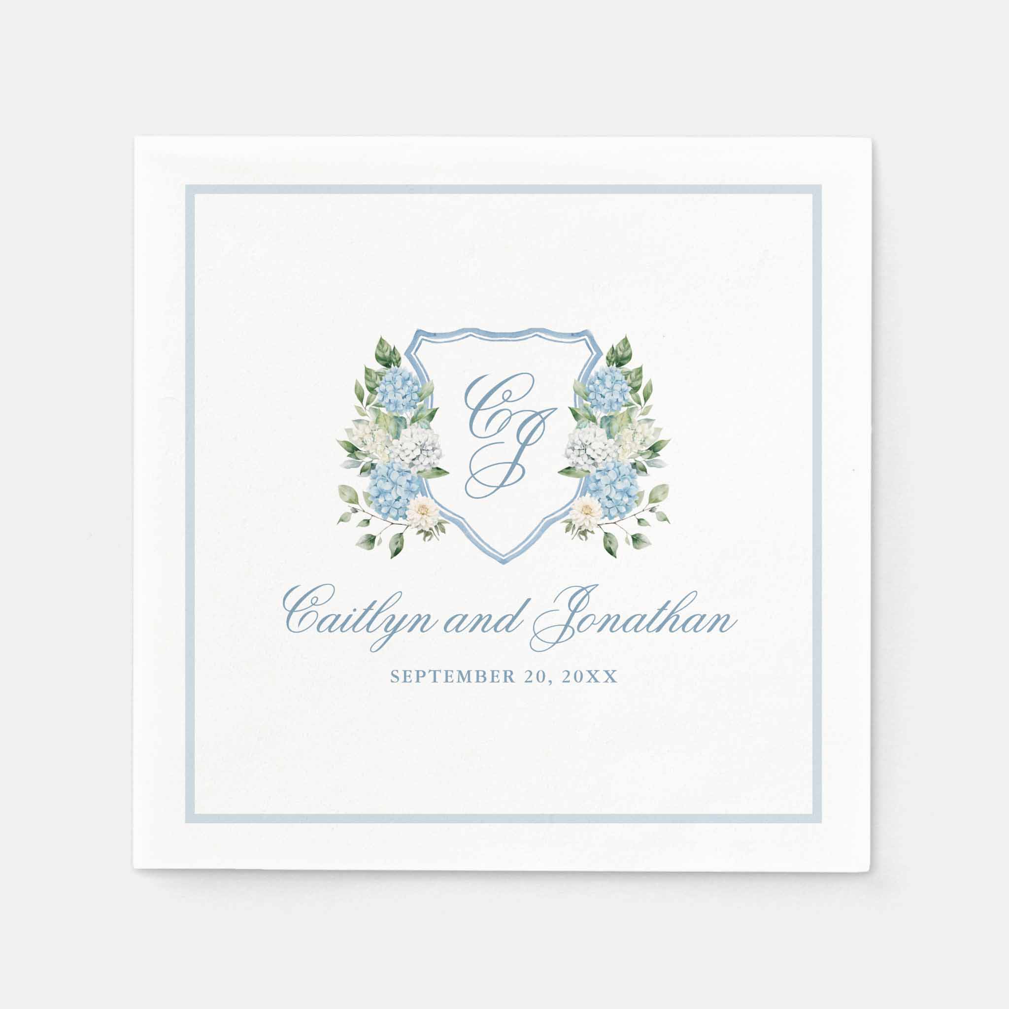 Square wedding napkin with blue hydrangea floral crest, script names and date, framed by a soft blue border.