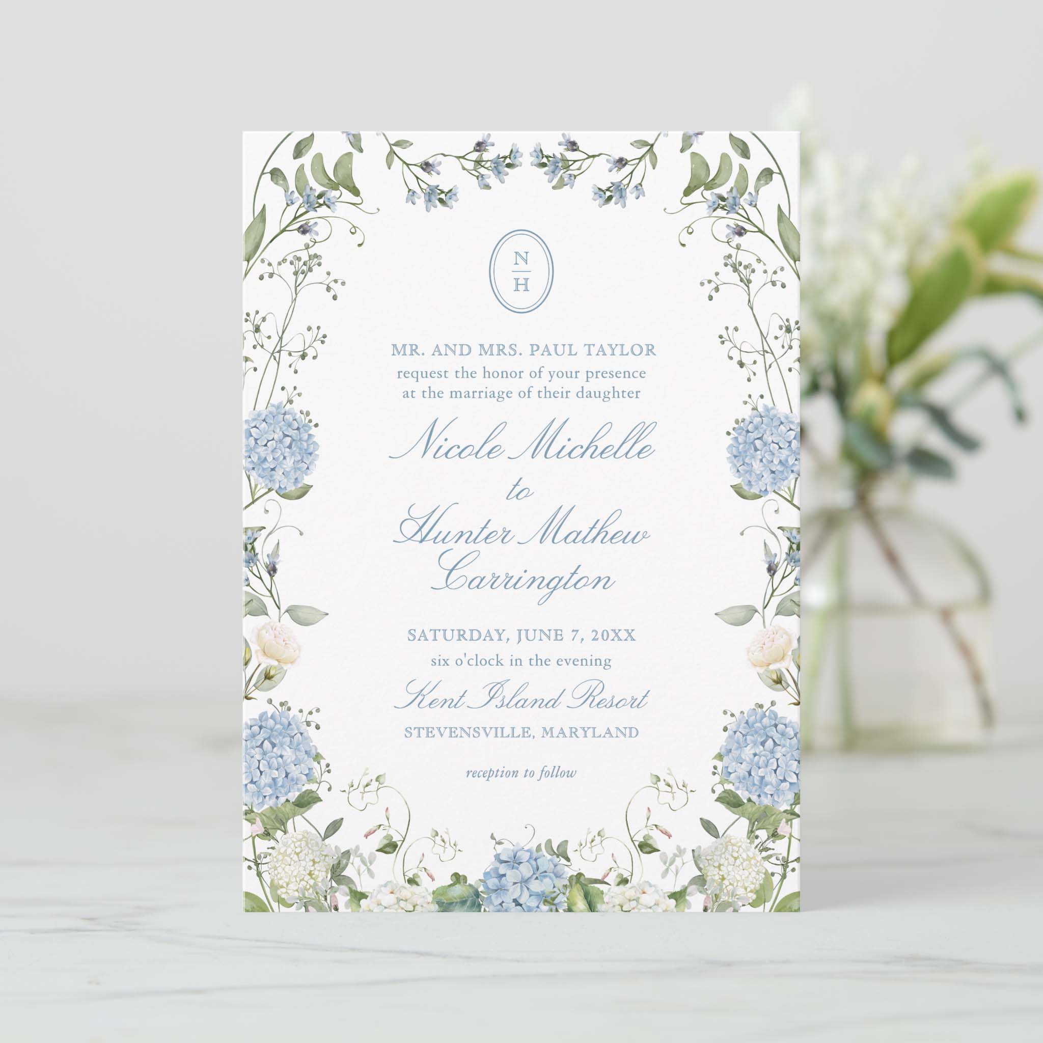 Blue hydrangea and greenery wreath wedding invitation with round monogram and classic serif text for a romantic ceremony.