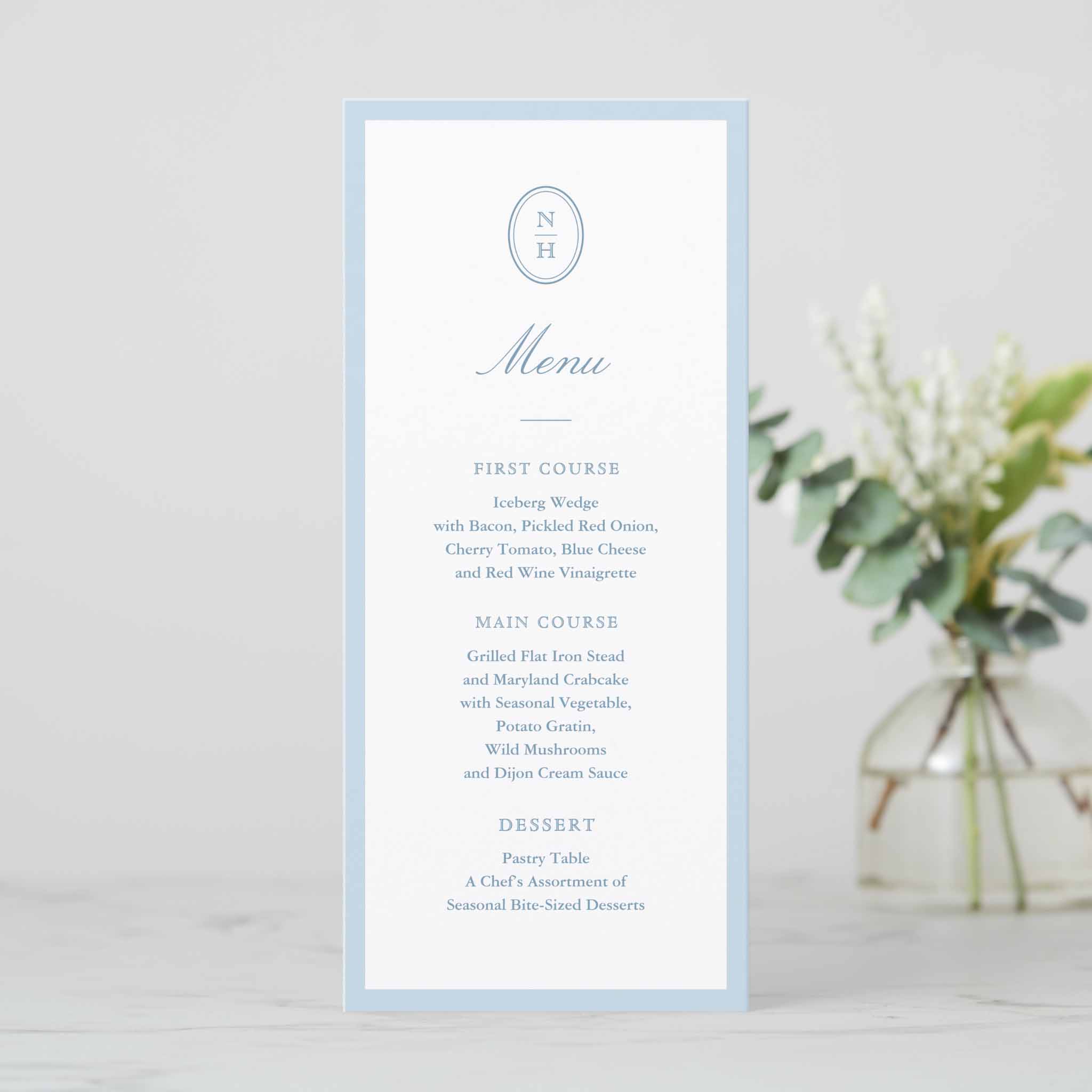 Tall dusty blue wedding menu card with simple monogram at the top, blue border and classic serif typography for first course, main course and dessert.